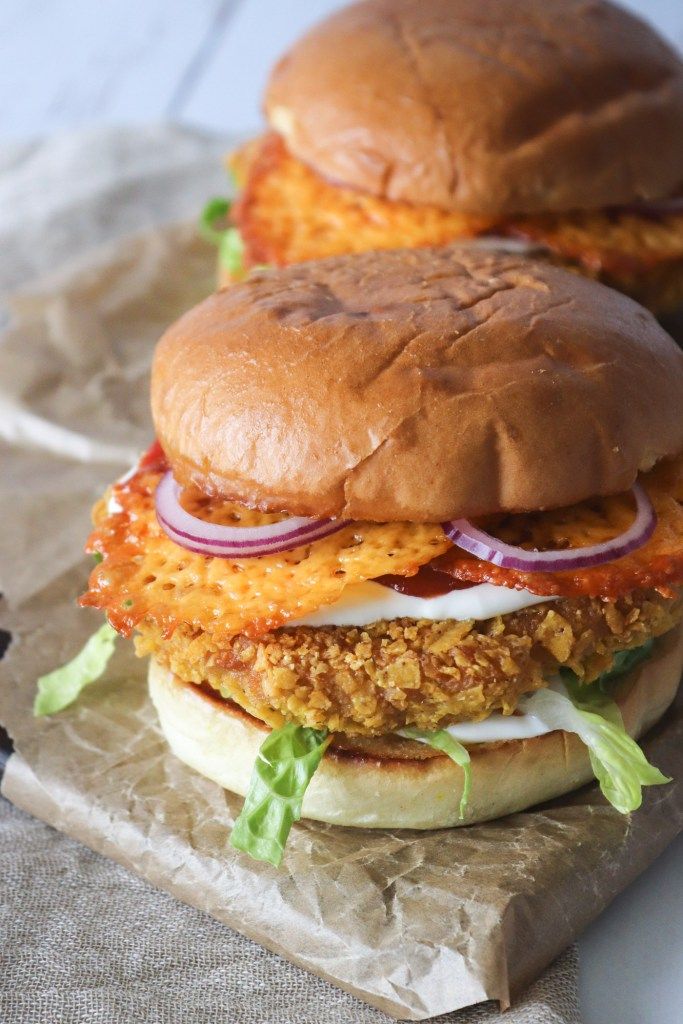 two chicken burgers with lettuce and onion on top sitting on wax paper