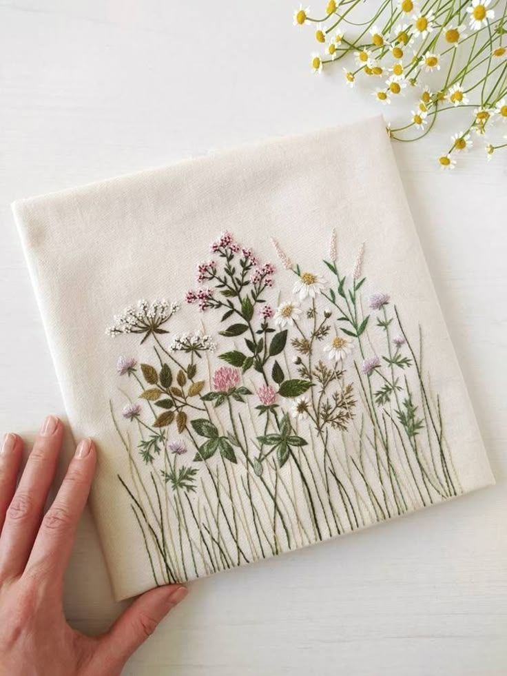 a hand is holding up a napkin with flowers on it and daisies in the background