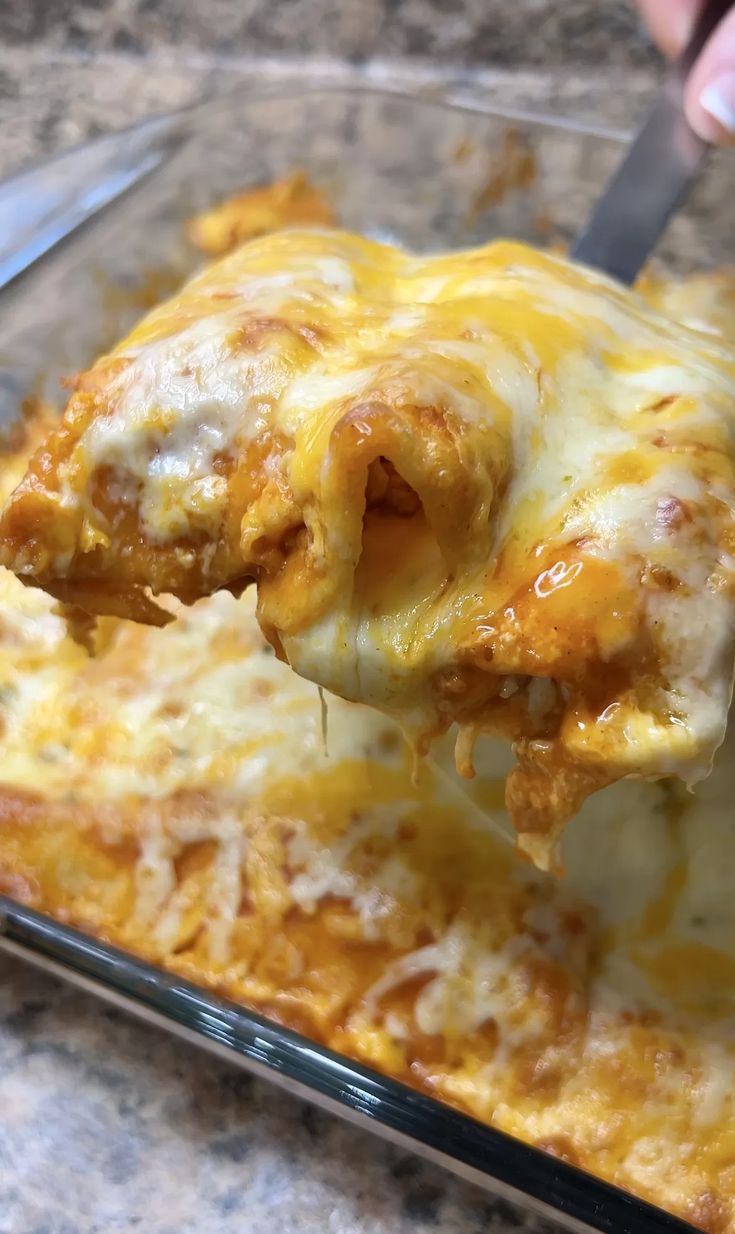 a person is taking a piece of lasagna from a casserole dish