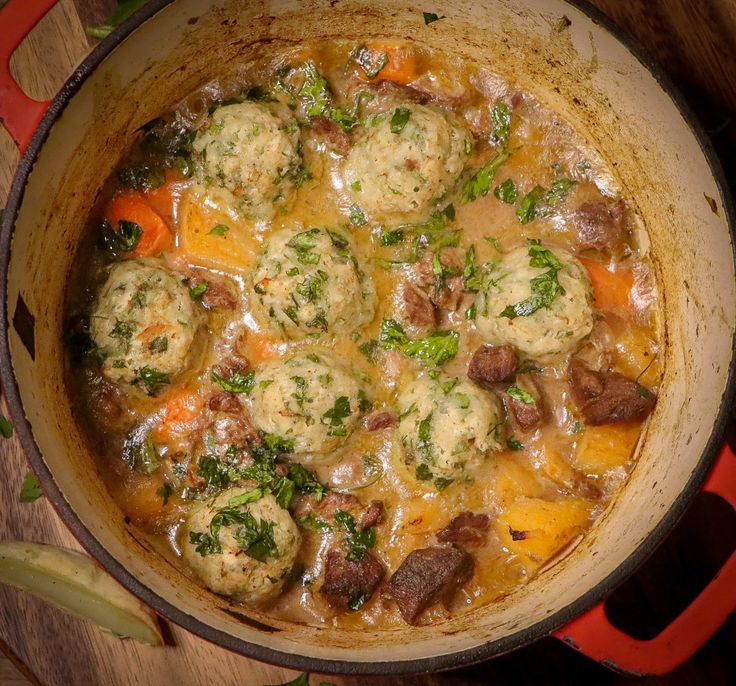 a pot filled with meatballs and vegetables on top of a wooden table