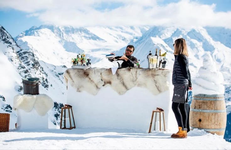 two people standing at a bar in the snow with mountains in the backgroud