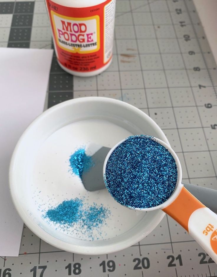 a white bowl filled with blue glitter next to a measuring ruler and bottle of modolode