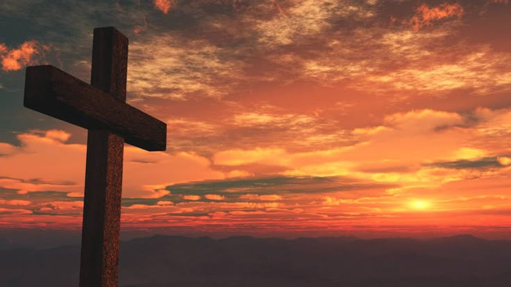 a wooden cross on top of a hill at sunset