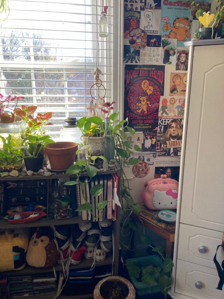 a room filled with lots of plants next to a white cabinet and window covered in posters