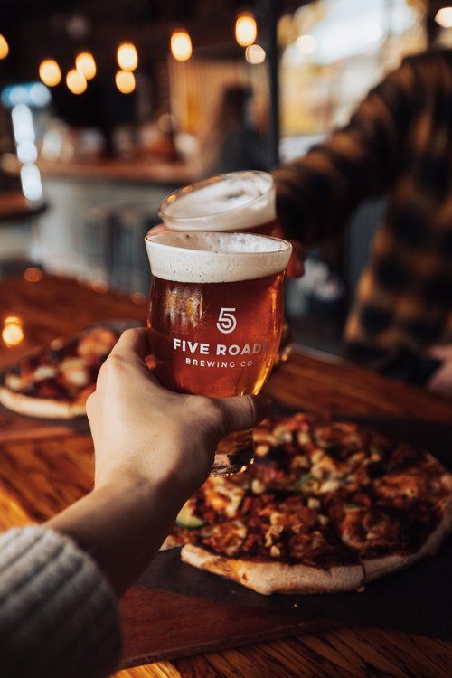 a person holding up a beer in front of a pizza on a wooden table at a restaurant