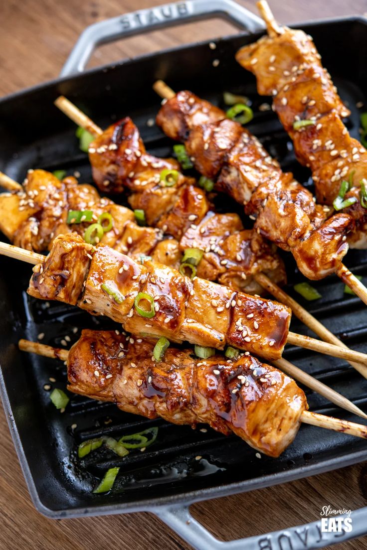 several skewers of chicken on a grill with green onions and scallions