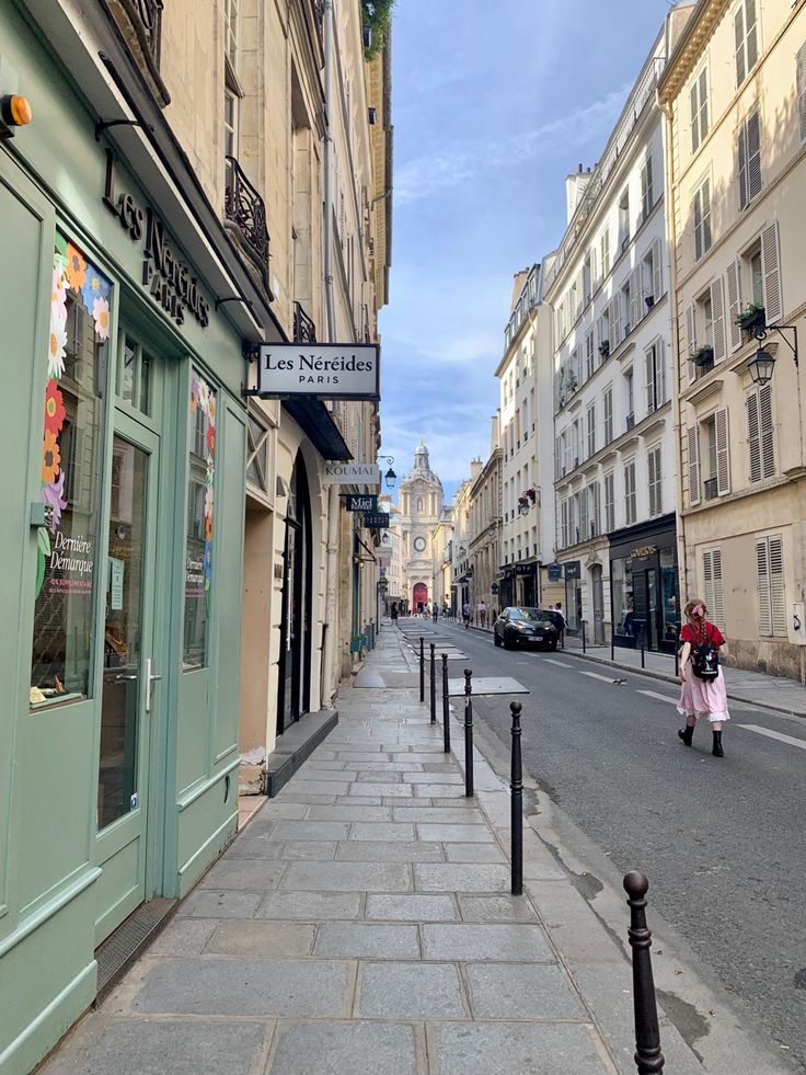 a woman walking down the street in front of some buildings with shops on each side