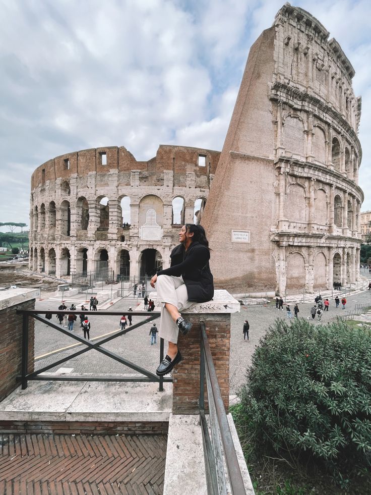 a woman sitting on top of a brick wall next to an old building and looking at the sky