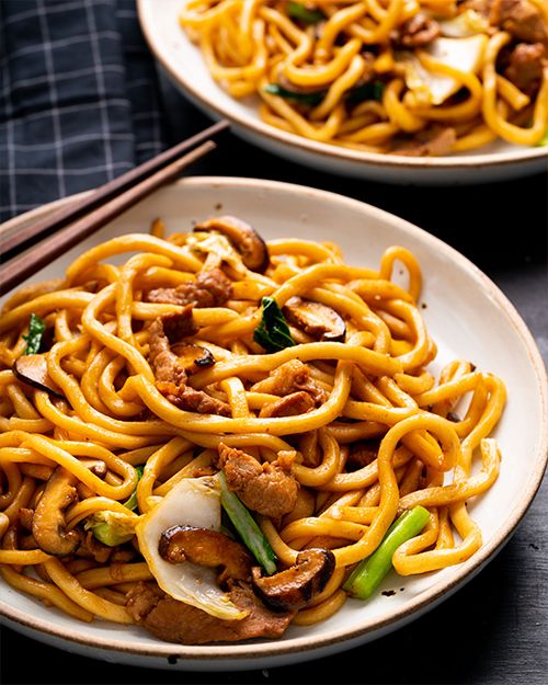 two plates of noodles with meat and vegetables on them, next to chopsticks