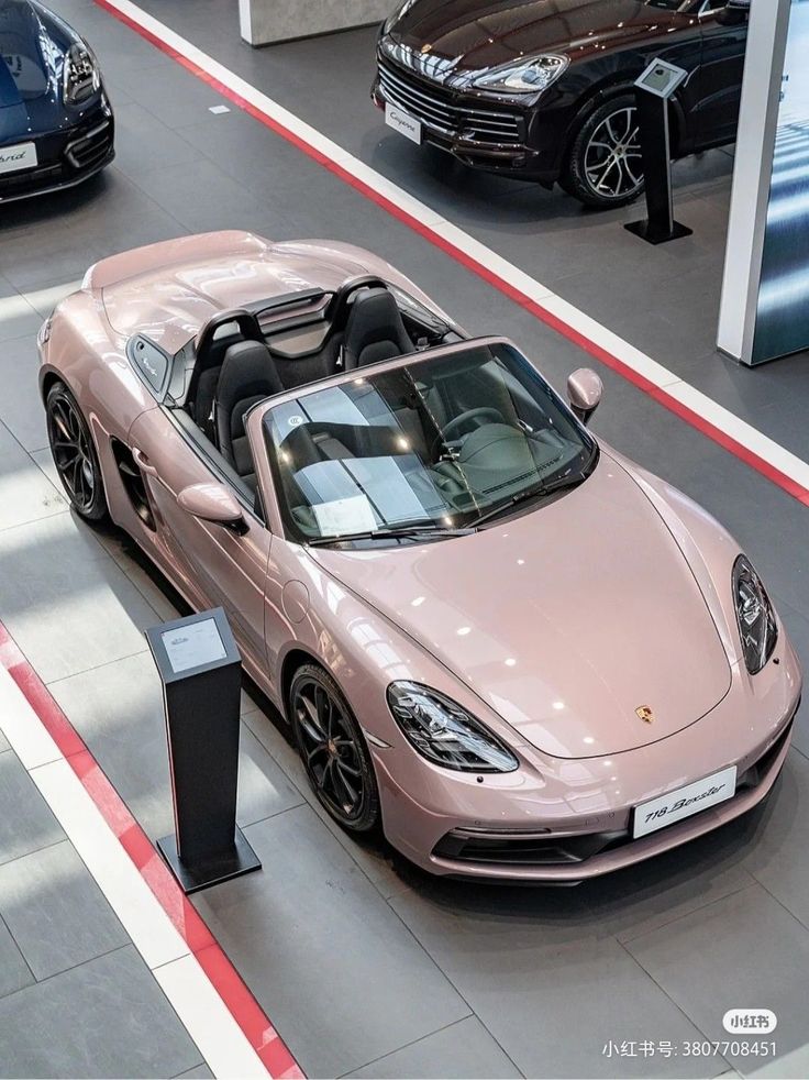 a pink sports car is parked in a showroom with other cars on the floor