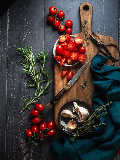 tomatoes and herbs are on a cutting board next to a knife, spoons and fork