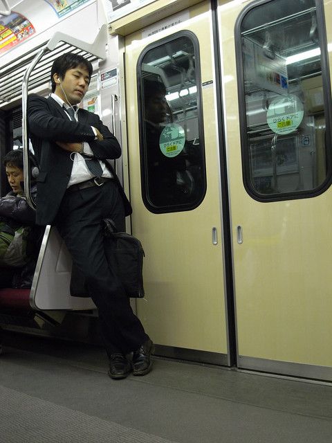 a man in a suit and tie standing on a subway train with his arms crossed