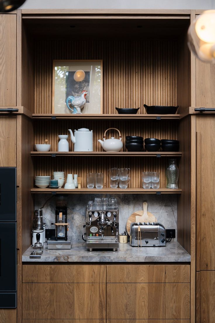 a kitchen with wooden cabinets and shelves filled with coffee pots, cups, and other items