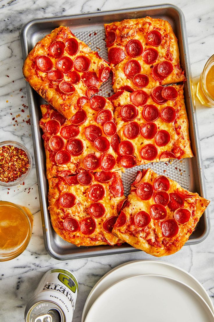 pepperoni pizza cut into four slices on a tray with beer and condiments