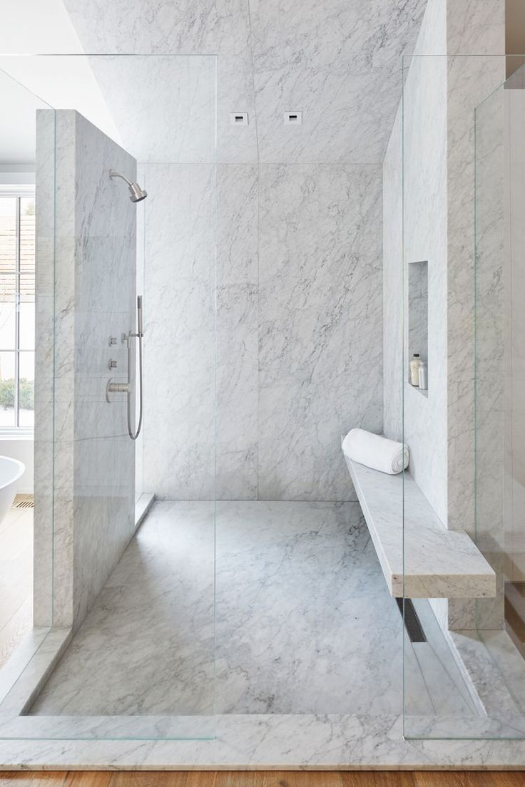 a bathroom with marble walls and flooring in the shower area, along with a bench