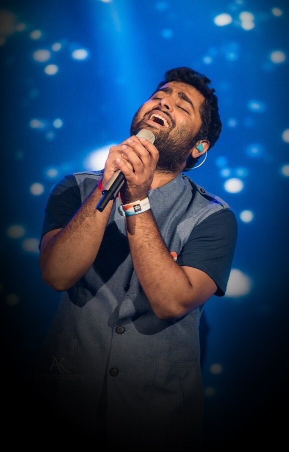 a man singing into a microphone while standing in front of a blue stage with lights