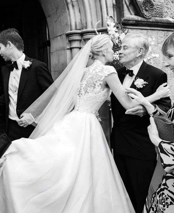 the bride and groom are hugging each other in front of an old building with people standing around