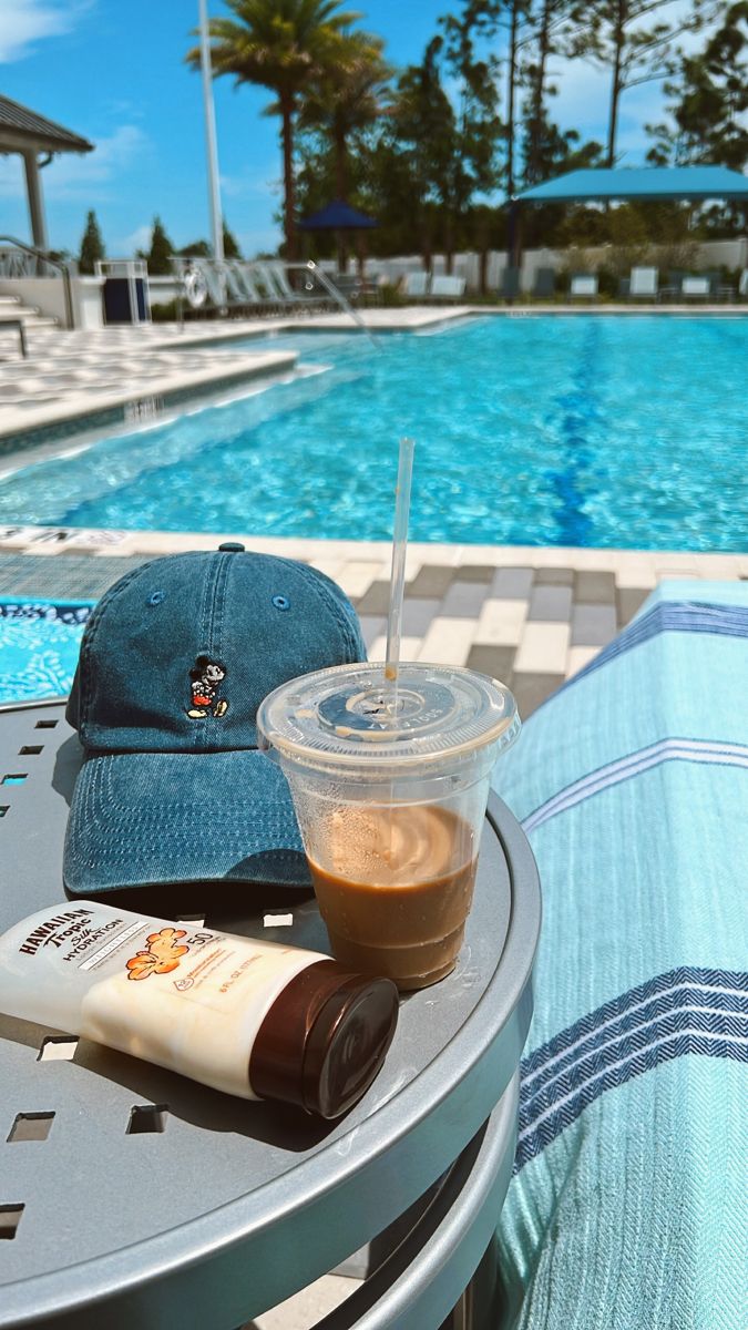 a cap and drink sitting on a table next to a swimming pool