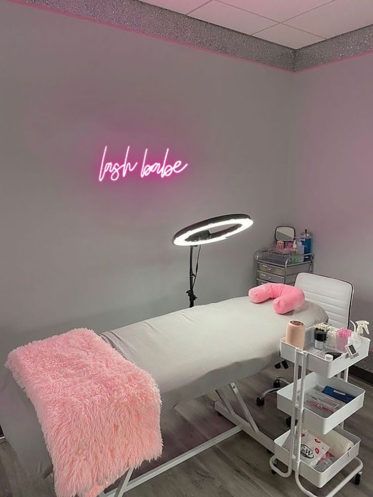 a pink neon sign above a bed in a room with grey walls and wood flooring