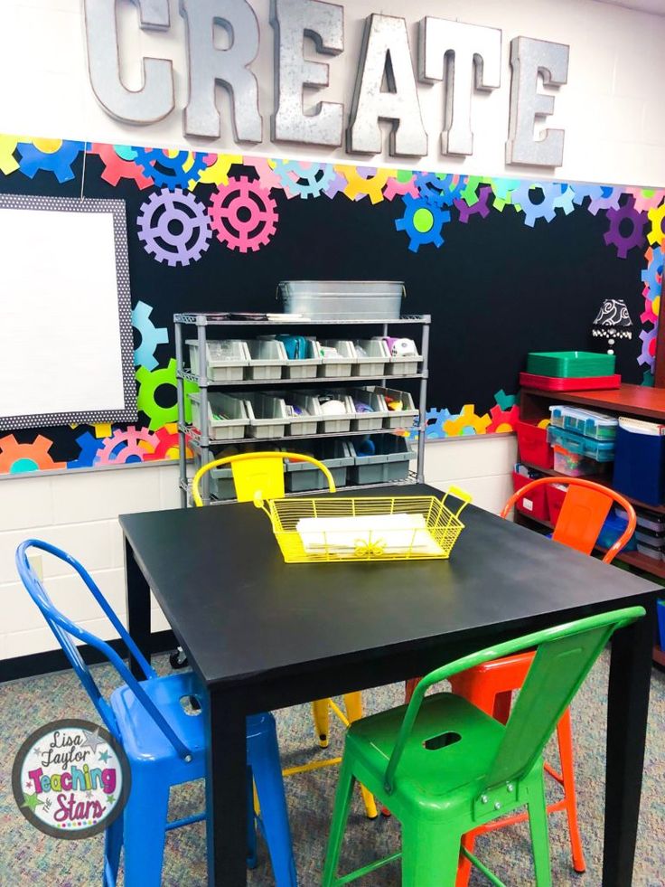 there is a black table with colorful chairs around it and a chalkboard on the wall