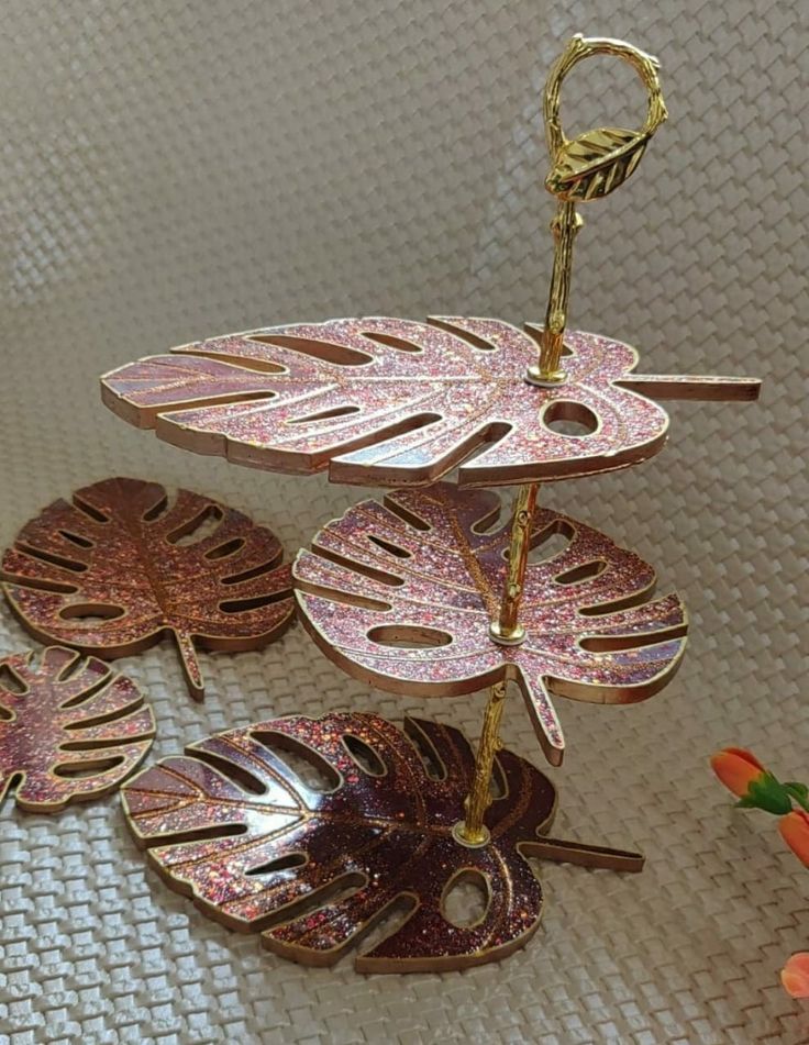 three leaf shaped brooches hanging from a hook on a white surface with flowers in the background