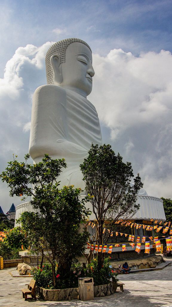 a large white buddha statue sitting in the middle of a park