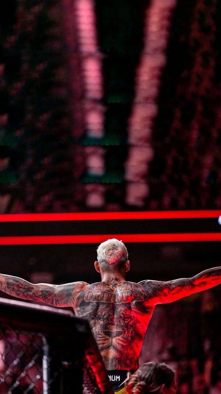 a man with tattoos on his back standing in the middle of a wrestling ring and holding his arms out