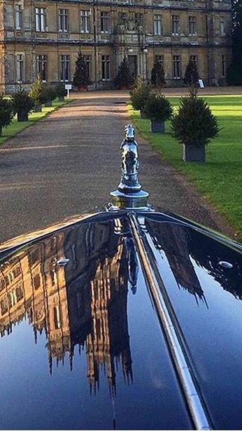 the reflection of a large building in the windshield of a classic car on a driveway