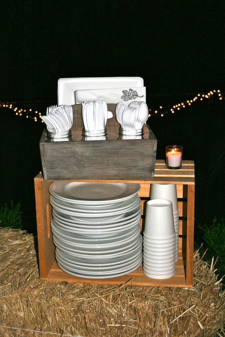 plates and cups are stacked on a wooden crate with string lights in the dark behind them