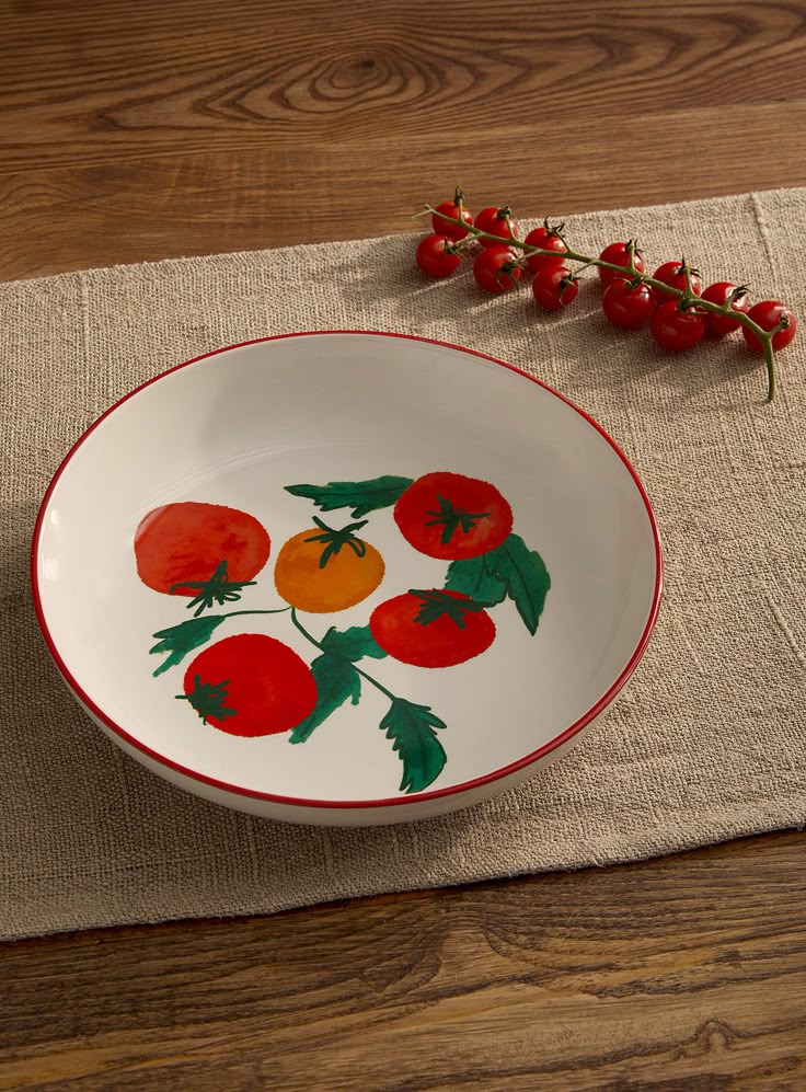 a bowl with tomatoes painted on it sitting on a placemat next to a plant