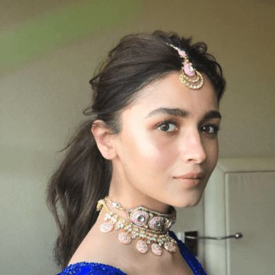 a woman in a blue dress with jewelry on her neck and shoulder, looking at the camera