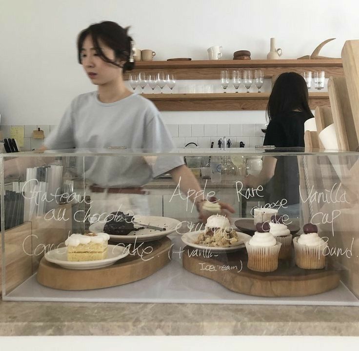 two people behind a counter with cakes and cupcakes