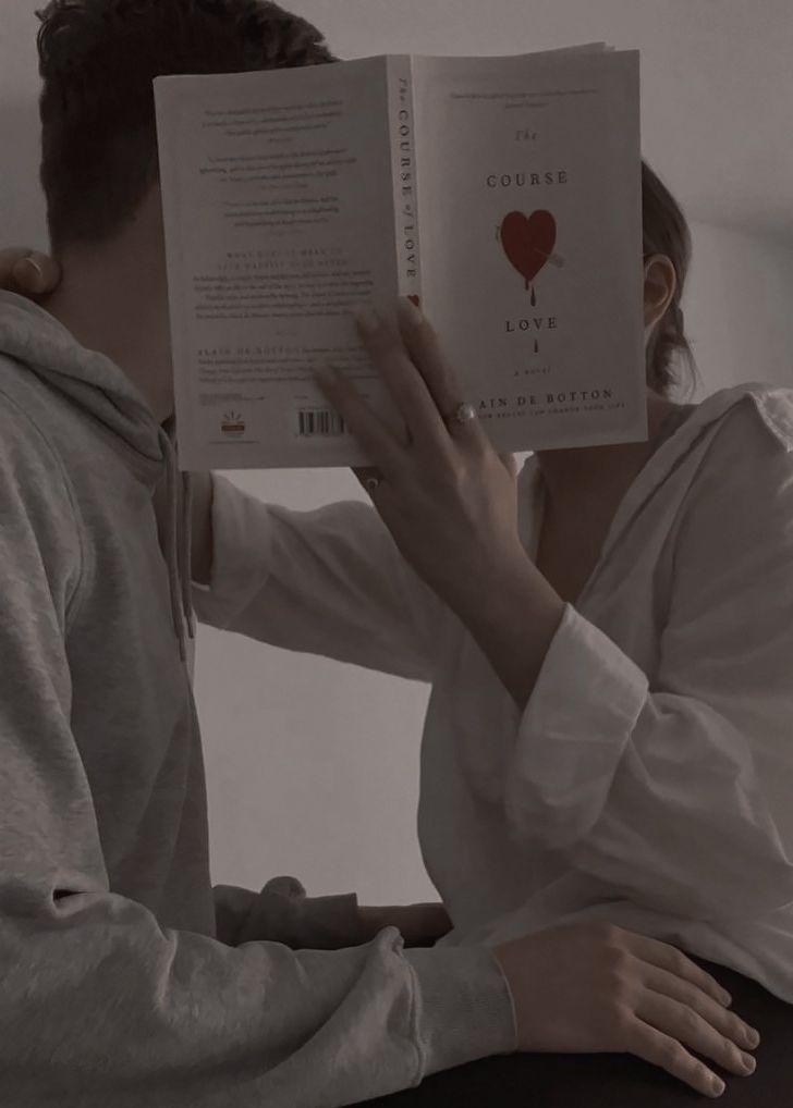 a man and woman sitting down reading a book with their faces close to each other