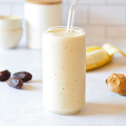 a smoothie in a glass with a straw is next to some fruit and nuts