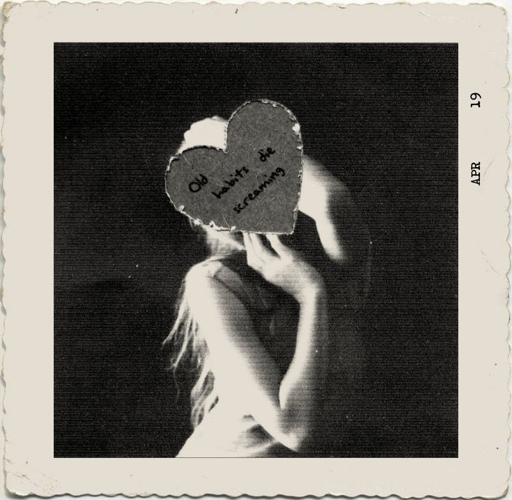 a black and white photo of a woman holding up a heart shaped paper cutout