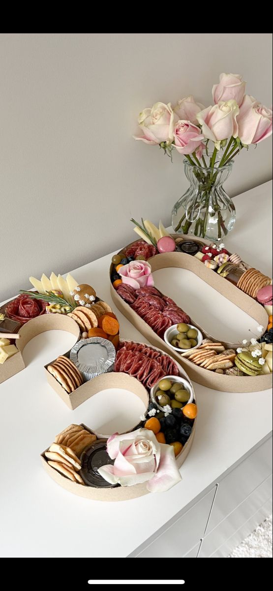 two trays filled with food sitting on top of a white counter next to flowers