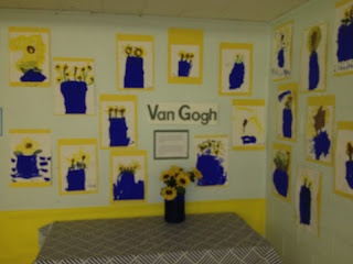 a room with yellow and blue wallpaper, pictures on the walls and flowers in a vase