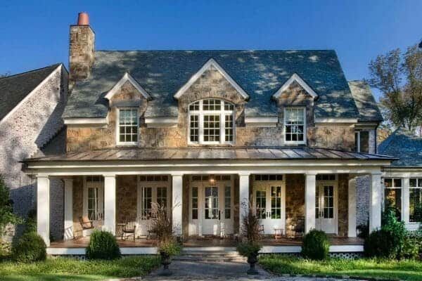 a large stone house with white trim and double doors on the front porch, surrounded by greenery