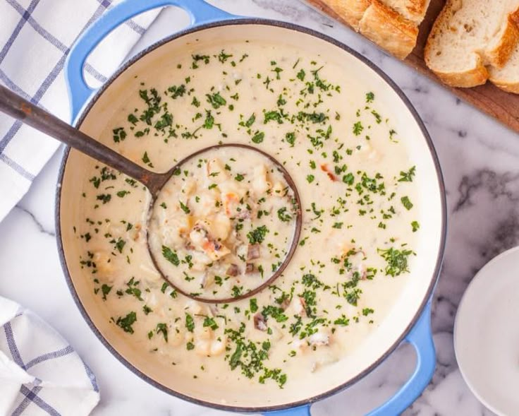 a blue pot filled with soup next to some bread on a cutting board and spoon