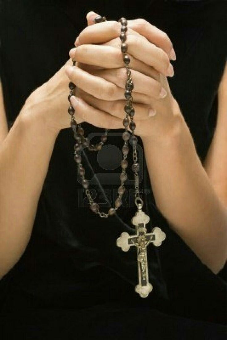 a woman wearing a black shirt and holding a rosary with her hands in front of her face