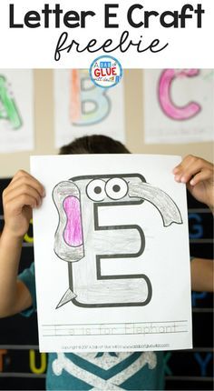 a young boy holding up a paper with the letter e drawn on it in front of him