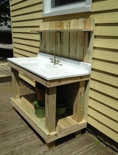 a sink sitting on top of a wooden table next to a building with yellow siding