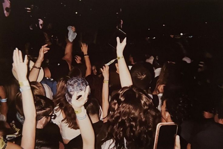 a group of people standing around each other at a concert with their hands in the air