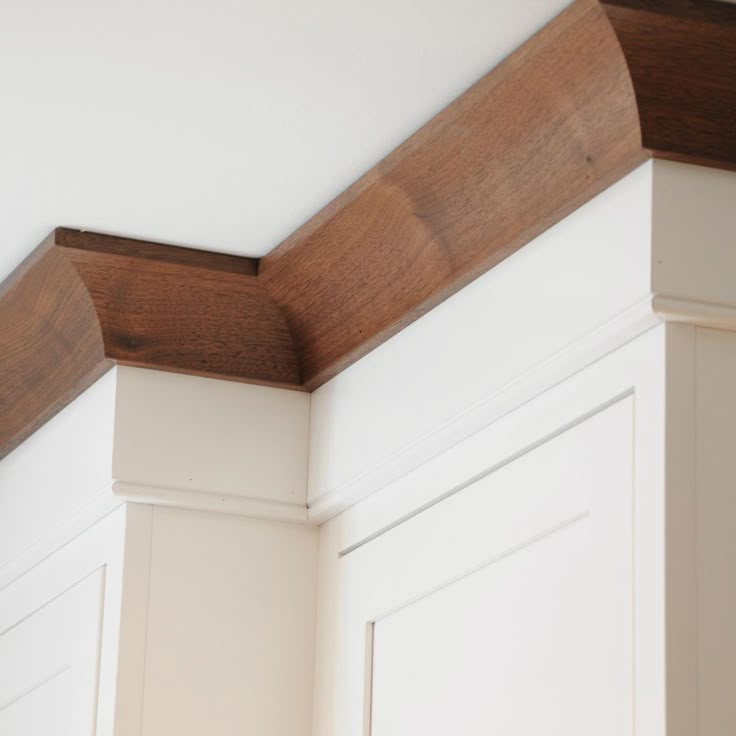 the corner of a kitchen with white cabinets and wood trim on the wall above it