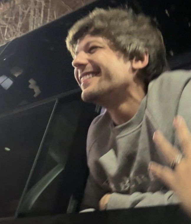 a man sitting in the back of a truck with his hand up and smiling at something