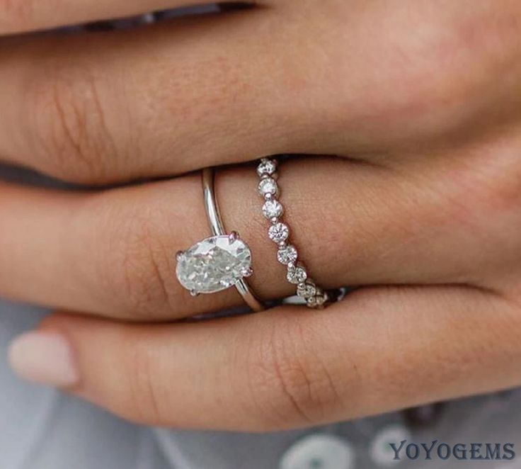 a woman's hand with a diamond ring on top of her finger and the other hand holding an engagement ring