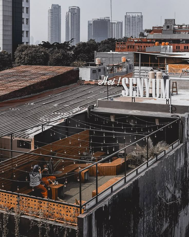 an industrial area with lots of buildings in the background and people sitting at tables on the roof