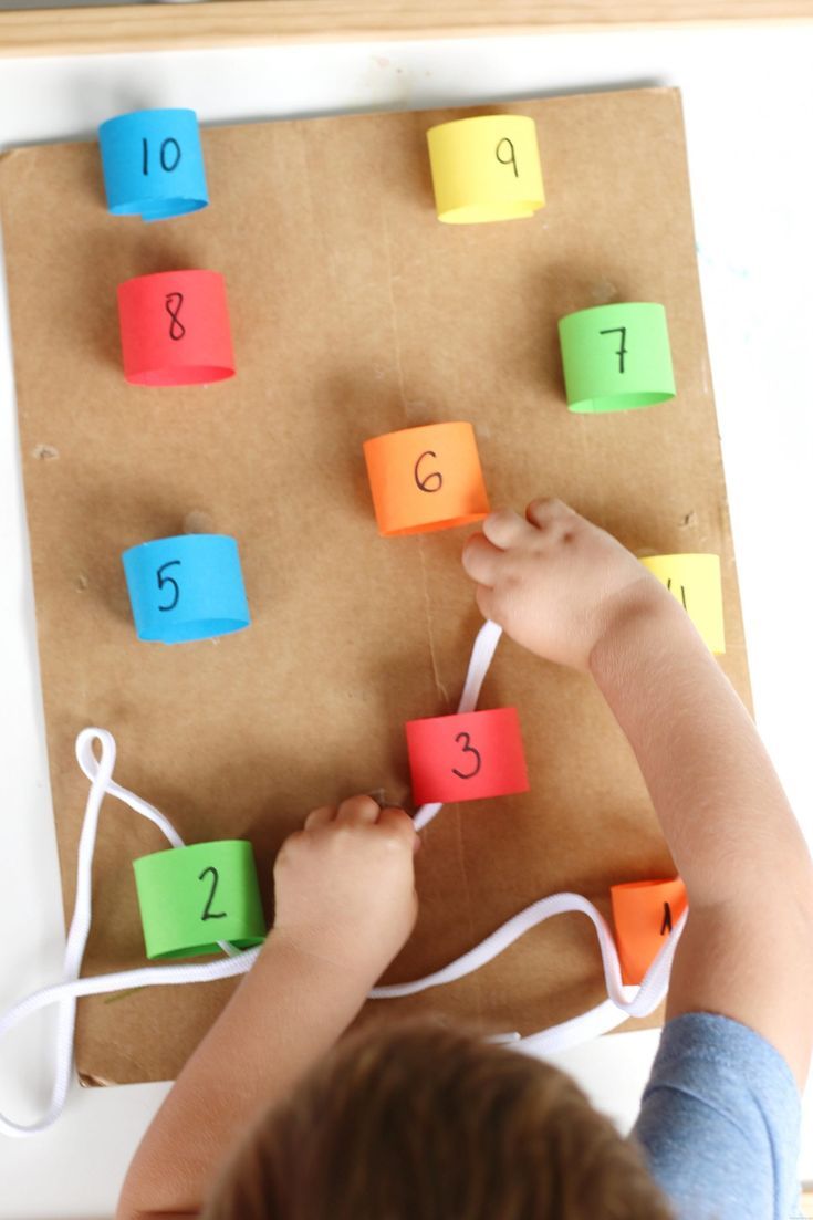 a young child playing with colored paper numbers on a piece of brown paper that is attached to a string