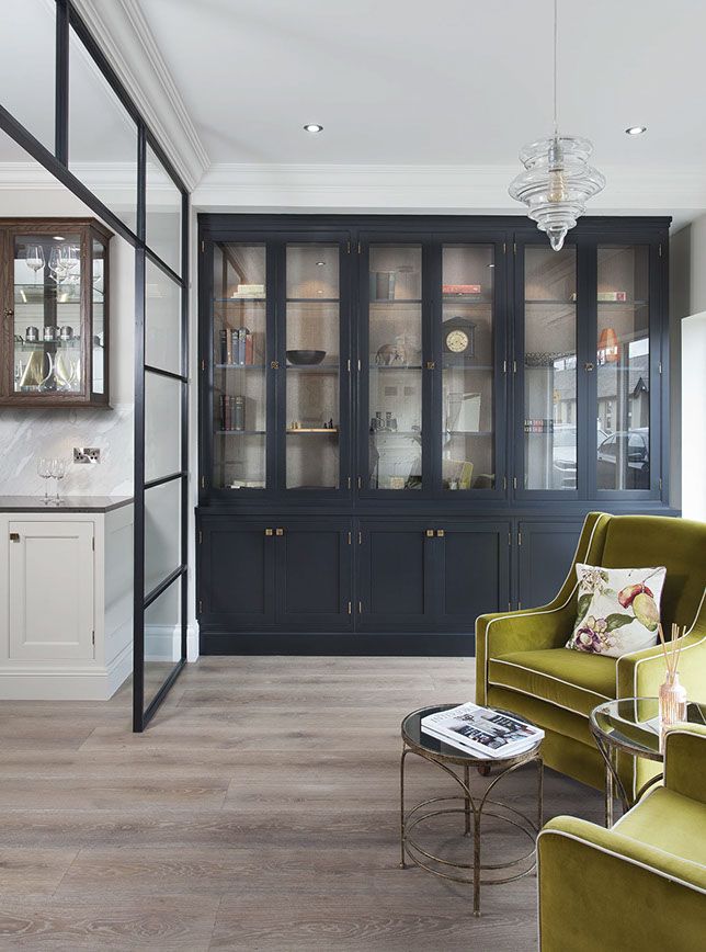 a living room filled with furniture next to a wall mounted book shelf and glass fronted cabinets