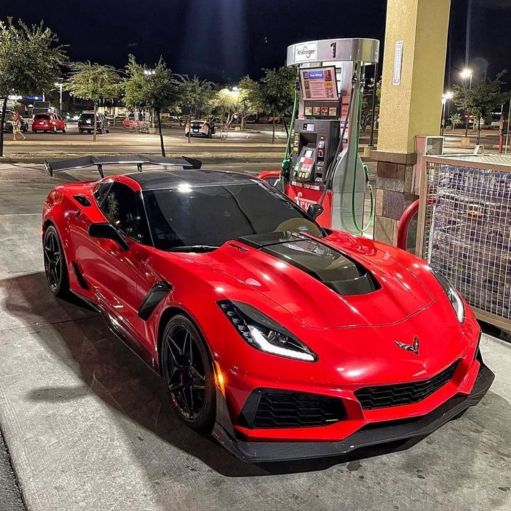 a red sports car parked in front of a gas station with its hood up and lights on